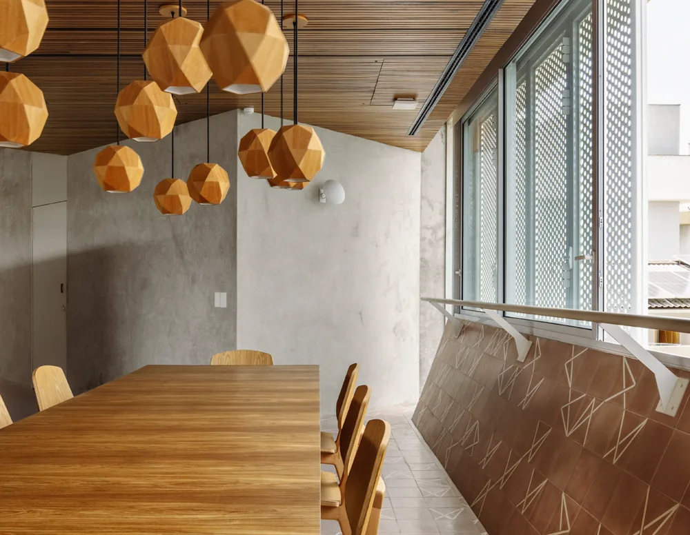 Sala de reuniões com mesa e pendentes de madeira e paredes de concreto